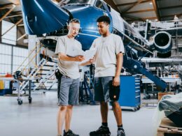 Two technicians review plans beside a blue aircraft inside a spacious hangar workshop