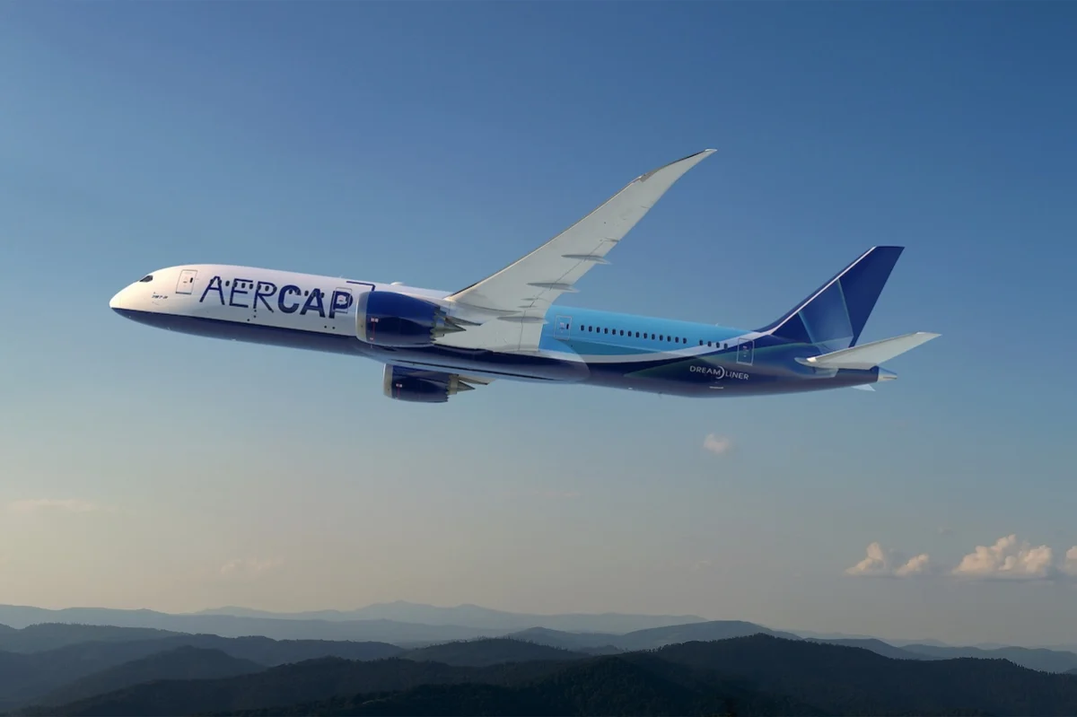 AerCap 787 9 Wide view of a blue and white aircraft labeled AER CAP in flight over a ridge of hills under a clear blue sky