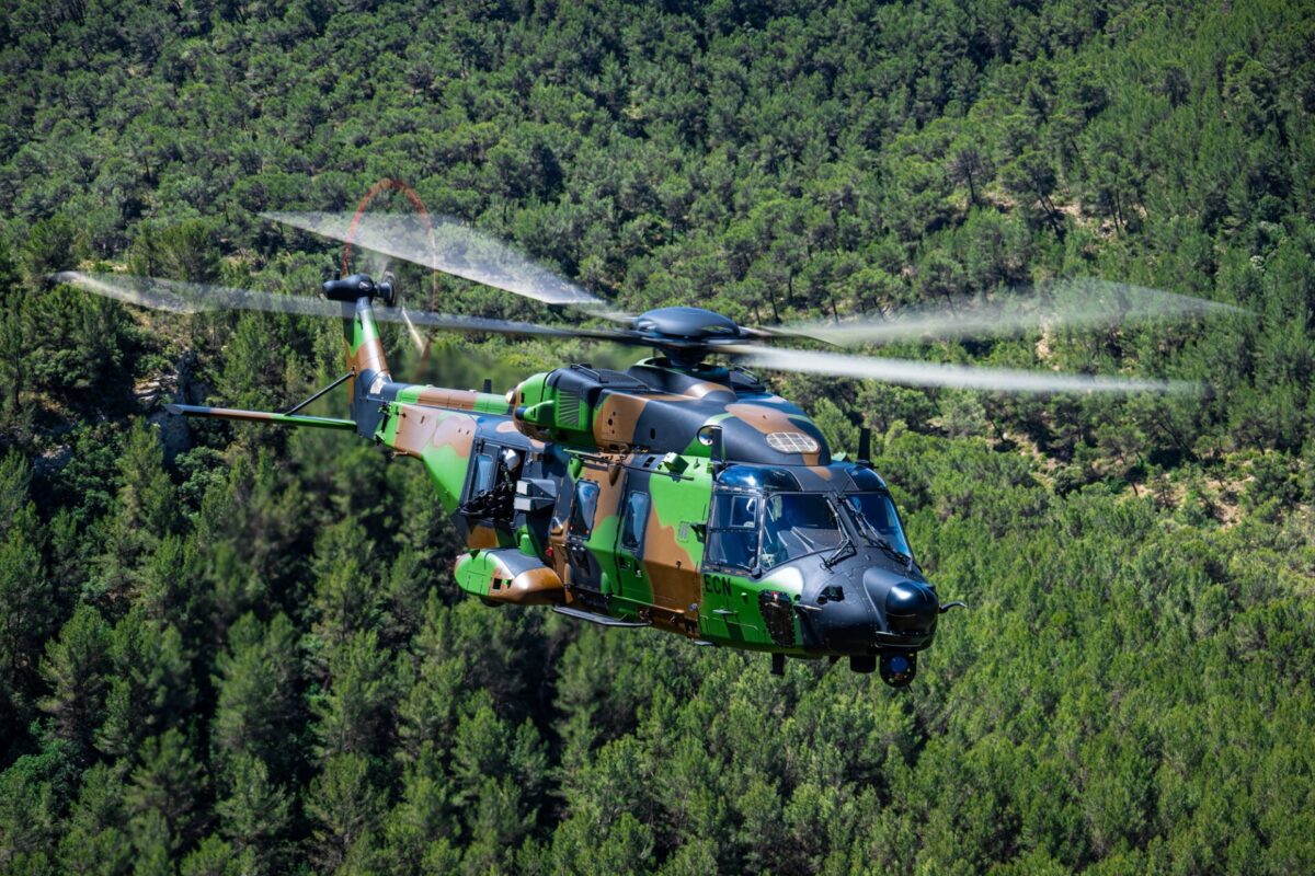 An Airbus Helicopters NH90 Standard 2 special operations helicopter Camouflage military helicopter in flight over a dense pine forest with blurred rotor blades