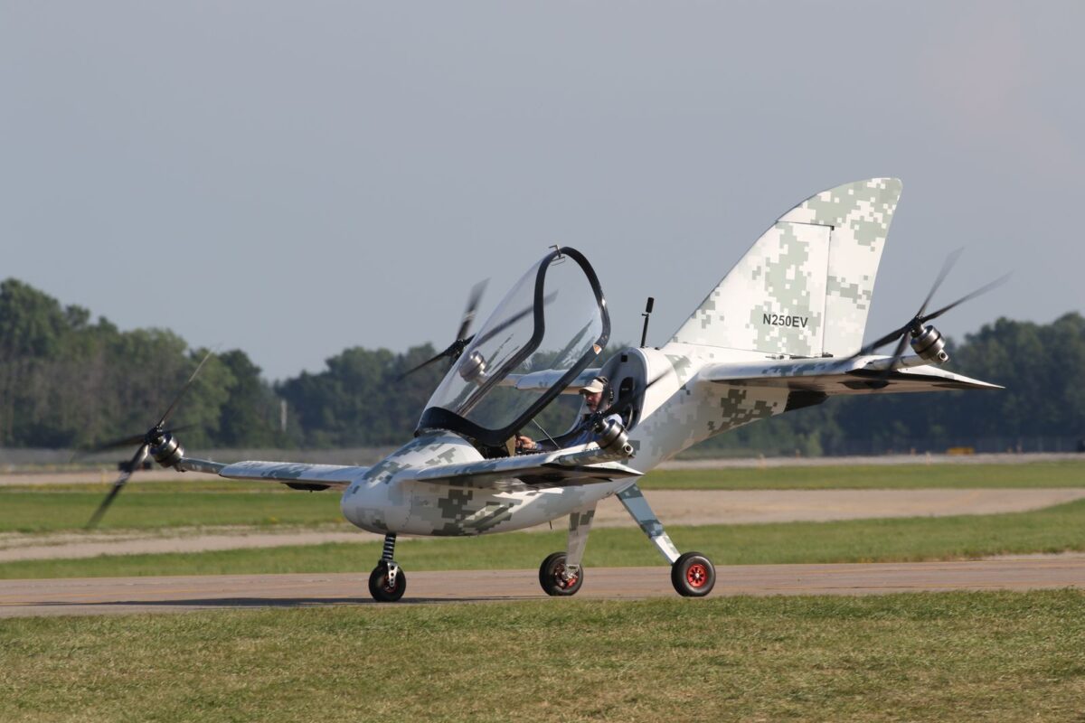 Axe Oshkosh Light camouflaged military style small aircraft on a runway with a two seat cockpit and open canopy taxiing or preparing for takeoff