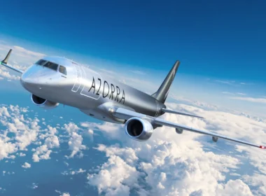 Silver passenger jet flying above fluffy clouds with 'AZORRA' branding on the fuselage, cruising in clear blue sky.