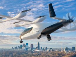 Futuristic white VTOL flying car labeled Bay Point hovering over a city skyline on a clear day