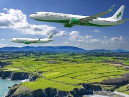 Two SMBC Aviation Capital airplanes fly in formation over a patchwork green farmland along a rocky coastline under a blue sky
