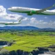 Two SMBC Aviation Capital airplanes fly in formation over a patchwork green farmland along a rocky coastline under a blue sky