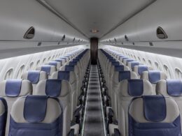 Inside an empty passenger airplane cabin facing the front rows of gray seats with blue headrests on both sides and a central aisle