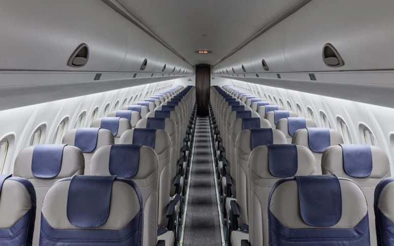 Inside an empty passenger airplane cabin facing the front rows of gray seats with blue headrests on both sides and a central aisle