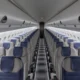 Inside an empty passenger airplane cabin facing the front rows of gray seats with blue headrests on both sides and a central aisle