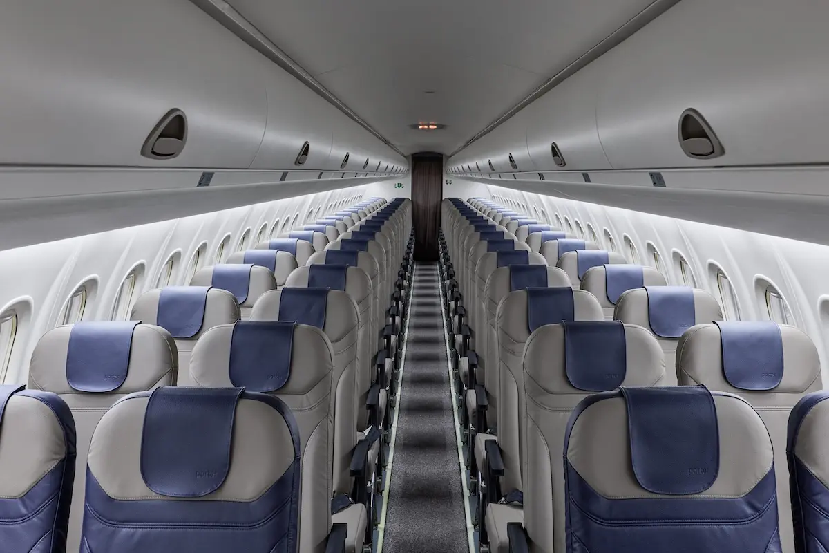 Inside an empty passenger airplane cabin facing the front rows of gray seats with blue headrests on both sides and a central aisle