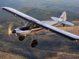 Small single engine light aircraft in flight over a forested valley with hills in the background