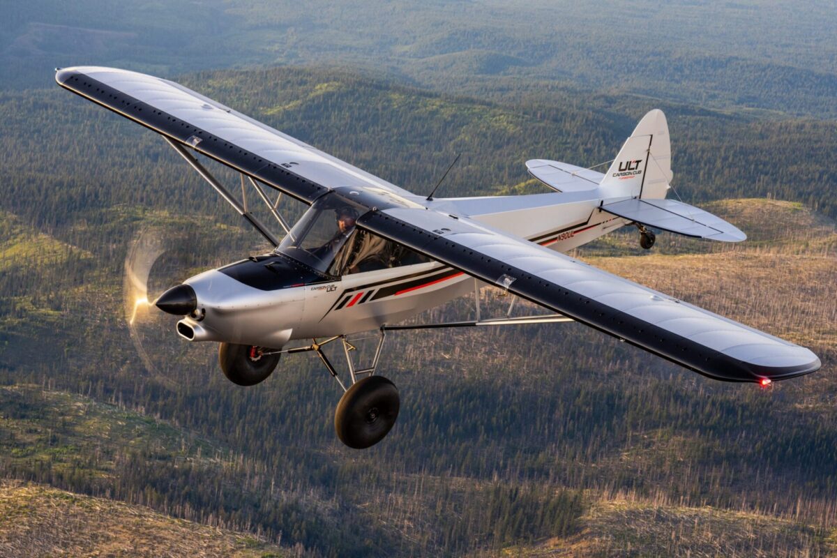 DSC00373 copy scaled Ultralight airplane cruising over a forested valley white and black fuselage with red accents propeller blurred from motion