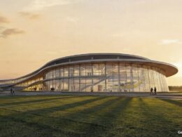 Modern glass walled pavilion with a curved roof at sunset people walking on adjacent paths and a grassy foreground