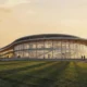 Modern glass walled pavilion with a curved roof at sunset people walking on adjacent paths and a grassy foreground