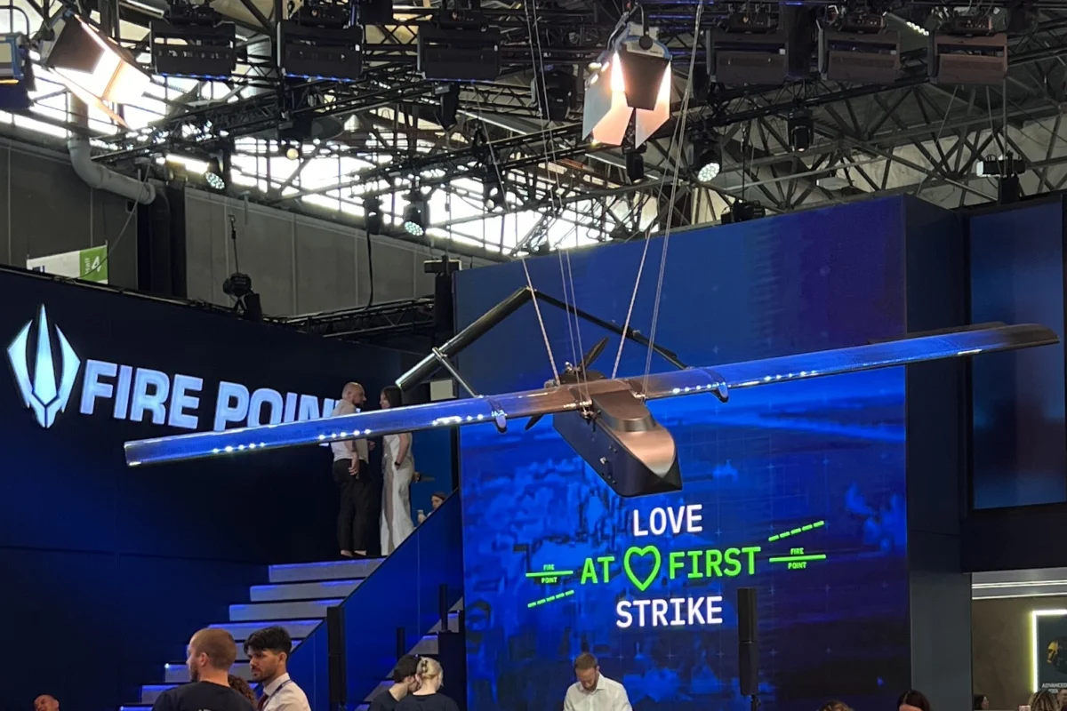 Fire Points upgraded FP 1 long range strike drone with its redesigned fuel carrying wing displayed at Eurosatory 2026 Suspended aircraft wing model overhead at a blue booth with a digital screen reading LOVE AT FIRST STRIKE and FIRE POINT branding