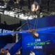 Suspended aircraft wing model overhead at a blue booth with a digital screen reading LOVE AT FIRST STRIKE and FIRE POINT branding