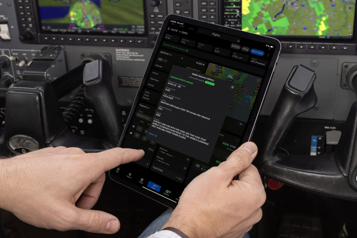 Pilot in cockpit holding a tablet showing flight plans and maps used to manage a flight