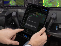 Pilot in cockpit holding a tablet showing flight plans and maps used to manage a flight
