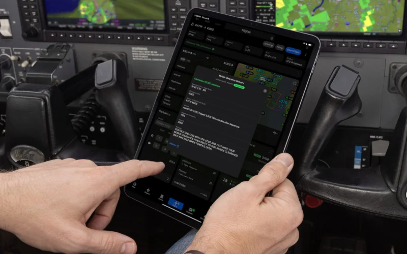 Pilot in cockpit holding a tablet showing flight plans and maps used to manage a flight