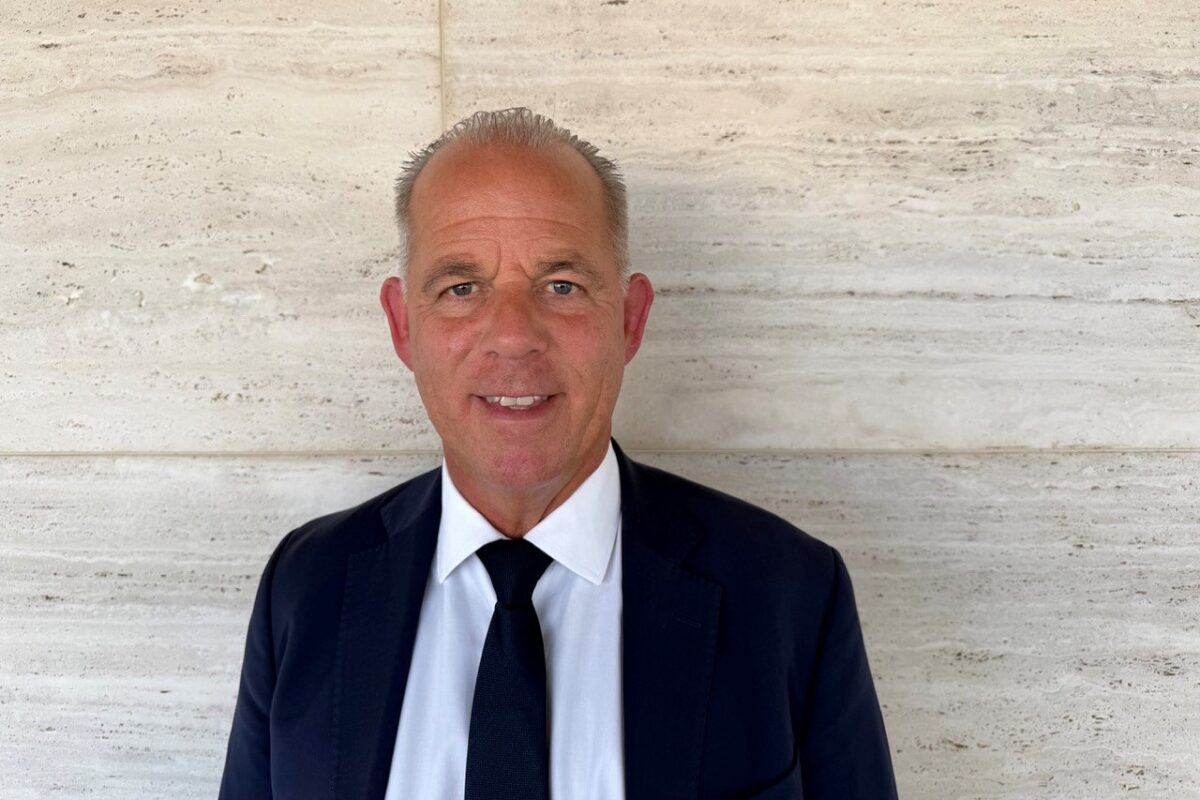 Gulf Air CEO Martin Gauss Smiling man in a navy suit and tie posing in front of a light stone wall portrait style image