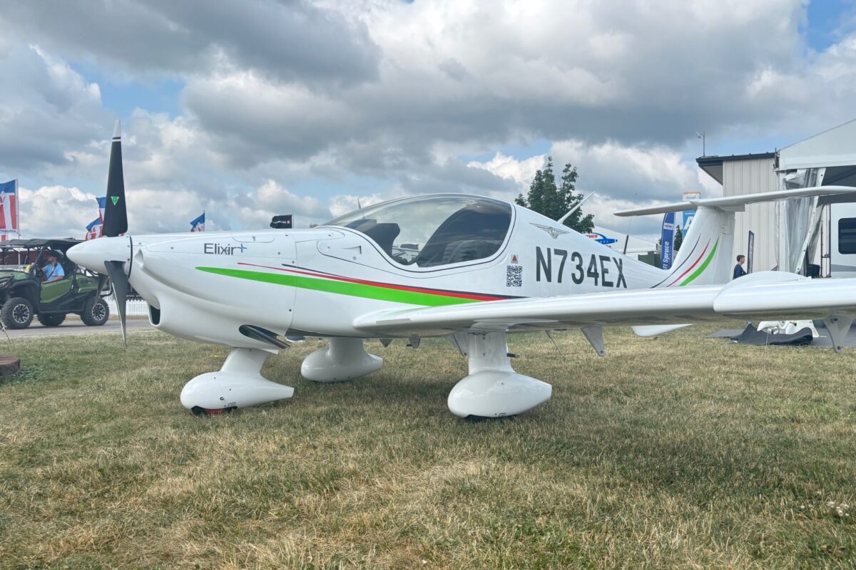 White single engine aircraft with green and red stripes on grass at an airshow tail number N734EX visible on fuselage Elixir