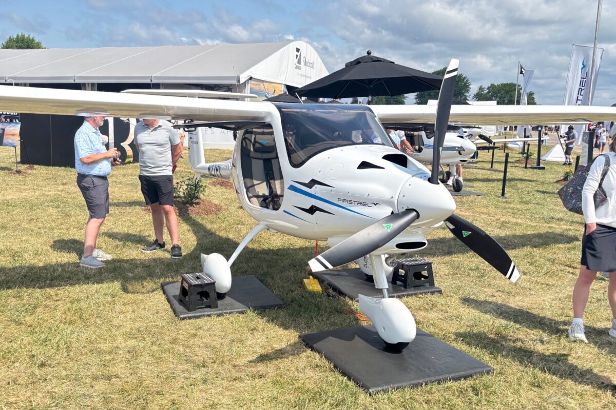 IMG 1296 Two men talking beside a white Pipistrel aircraft on display at an outdoor aviation expo with tents and attendees in the background