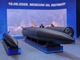Exhibition display a large dark missile on a stand with two suited figures discussing it blue backdrop reading 18062026 MOSCOW OIL REFINERY