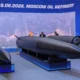 Exhibition display a large dark missile on a stand with two suited figures discussing it blue backdrop reading 18062026 MOSCOW OIL REFINERY