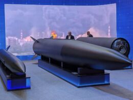 Exhibition display a large dark missile on a stand with two suited figures discussing it blue backdrop reading 18062026 MOSCOW OIL REFINERY