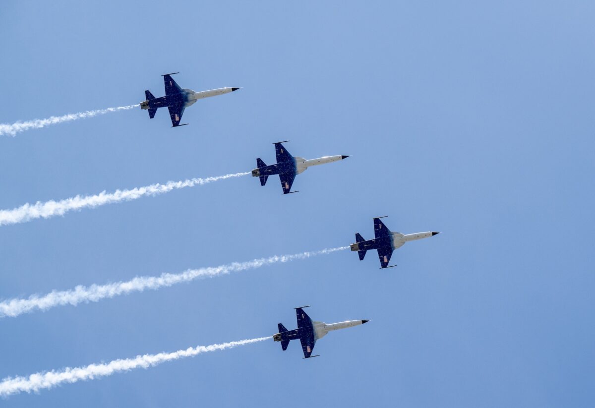 NASA at the Great American State Fair Four blue fighter jets fly in a tight formation across a clear blue sky leaving white smoke trails behind them at an airshow