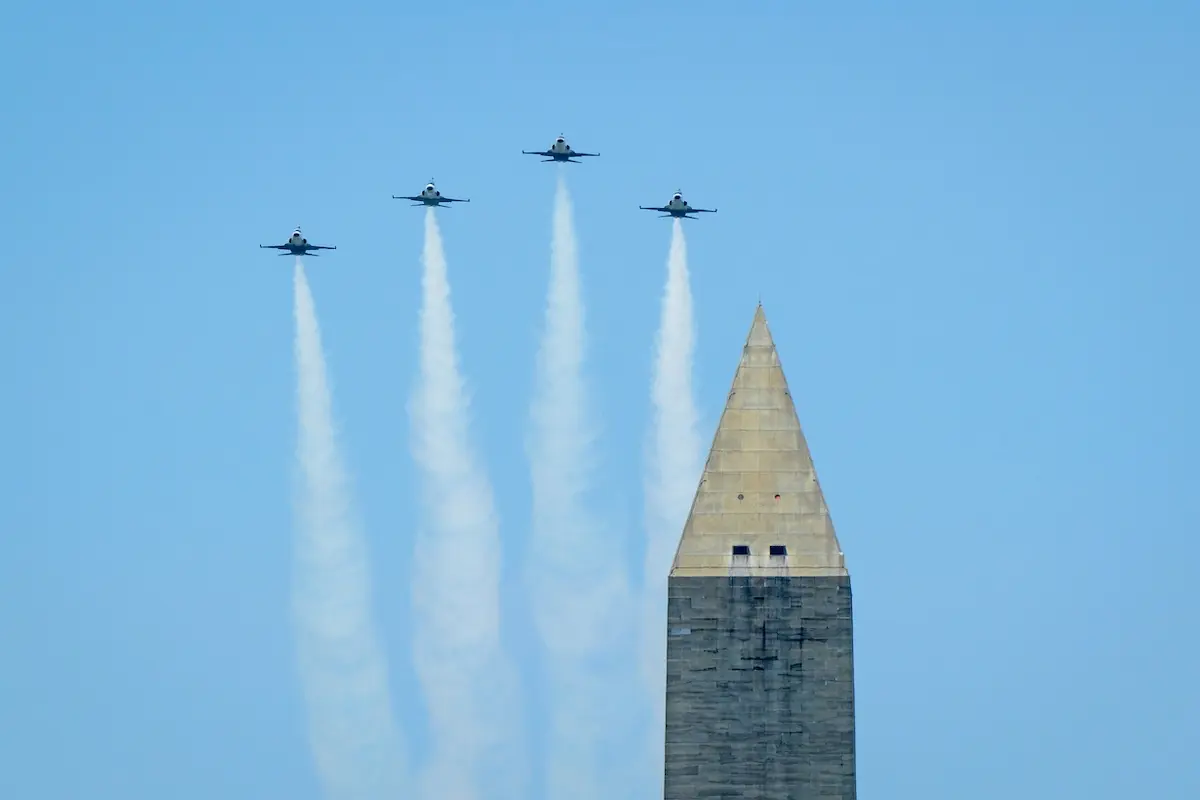 NASA at the Great American State Fair Four jets fly in tight formation over a tall obelisk leaving white smoke trails against a clear blue sky