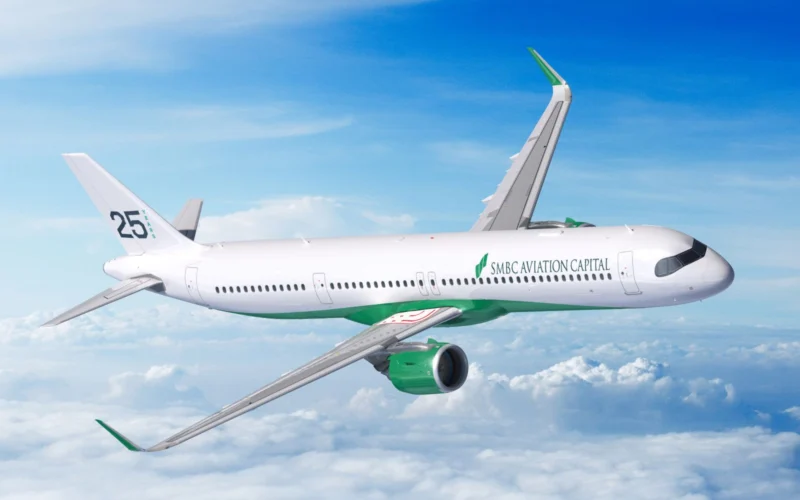White commercial airplane with green accents and SMBC Aviation Capital logo in flight above clouds