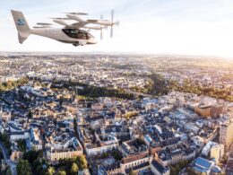 Sigma Air Mobility eVTOL aircraft flying over a dense cityscape at sunset with rotors spinning above rooftops