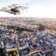 Sigma Air Mobility eVTOL aircraft flying over a dense cityscape at sunset with rotors spinning above rooftops