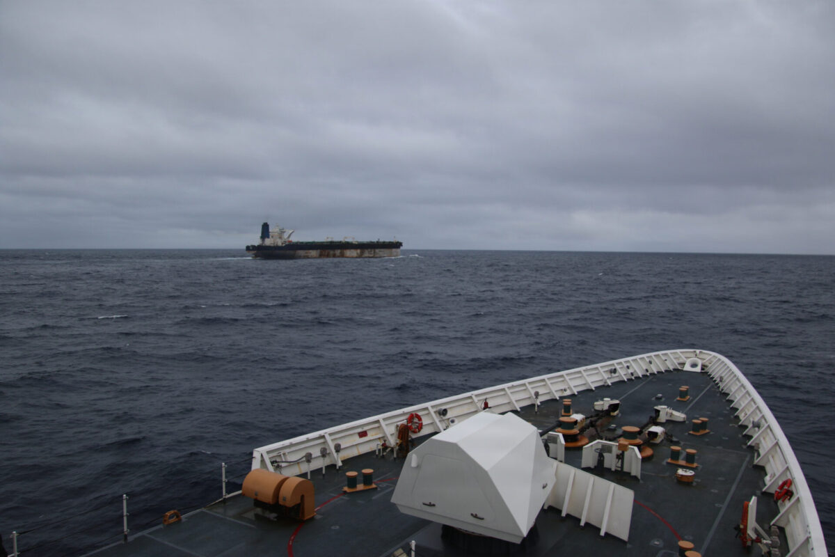 USCGC Munro conducts maritime operations in support of MV Bella 1 seizure Overcast ocean scene with a distant cargo ship on the horizon viewed from a ships deck with foreground deck equipment visible