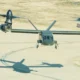 Twin engine tilt rotor aircraft Osprey on a runway with rotors extended preparing to land its shadow is visible on the tarmac