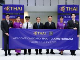 Group of six individuals in formal attire posing behind a large THAI banner at a THAI event Amsterdam welcome sign visible