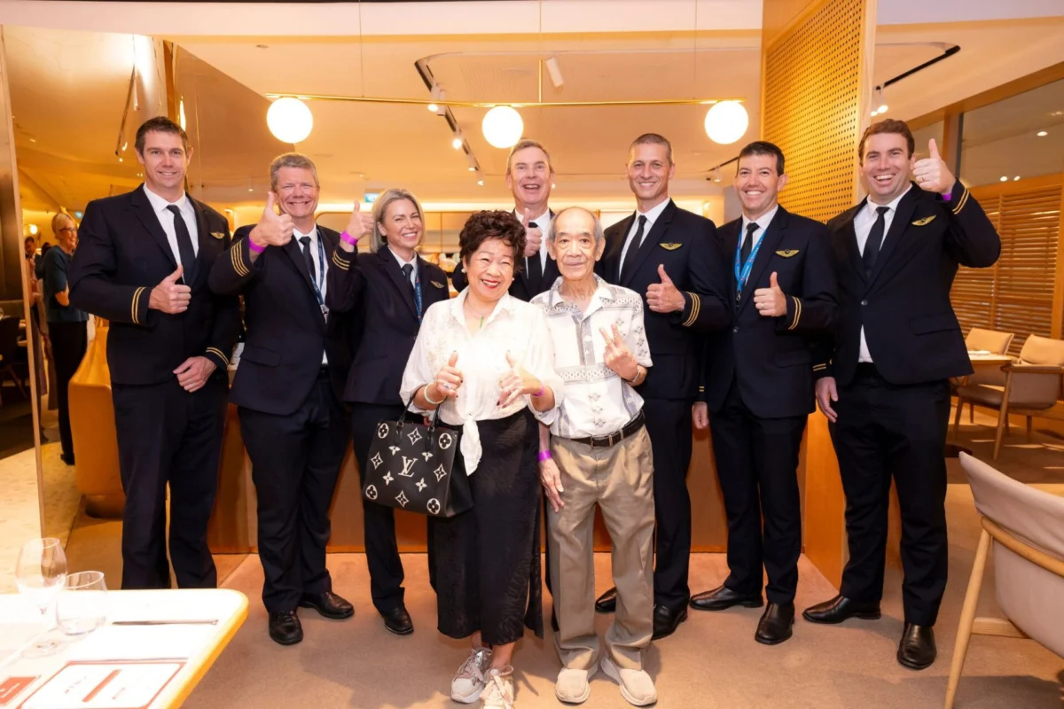 Qantas adds beloved restaurants dishes to Changi lounges Group of staff in navy uniforms with gold stripes pose with two smiling elderly guests all giving thumbs up in a warmly lit restaurant setting