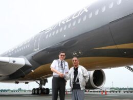 Two men shake hands in front of a large StarLux airplane on the tarmac one in a uniform