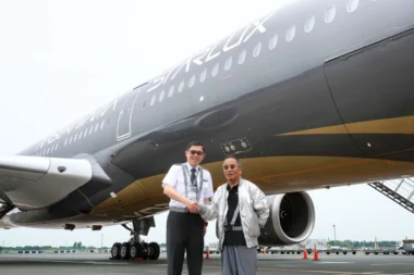 Two men shake hands in front of a large StarLux airplane on the tarmac one in a uniform