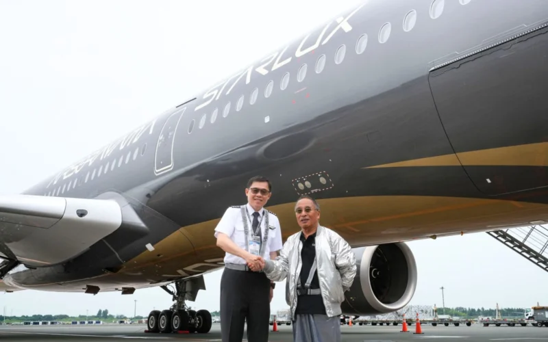 Two men shake hands in front of a large StarLux airplane on the tarmac one in a uniform