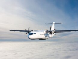 White twin engine propeller airplane flying above a sea of clouds against a blue sky viewed from the front