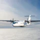 White twin engine propeller airplane flying above a sea of clouds against a blue sky viewed from the front