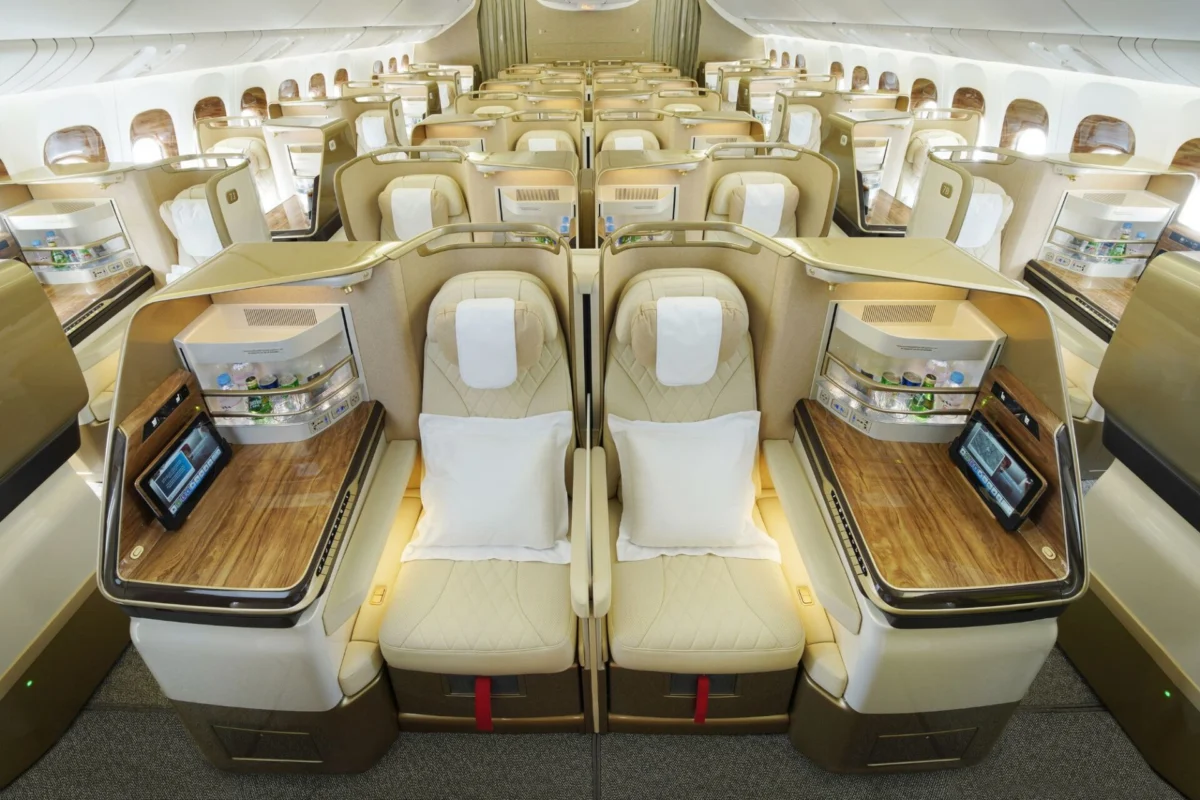 Luxurious business class airplane cabin with beige lie flat seats in private pods and wood topped desks along a central aisle
