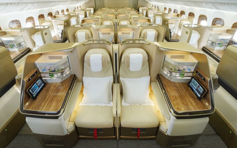 Luxurious business class airplane cabin with beige lie flat seats in private pods and wood topped desks along a central aisle