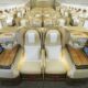 Luxurious business class airplane cabin with beige lie flat seats in private pods and wood topped desks along a central aisle