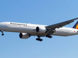 Wide view of a Philippines Airlines jet with landing gear extended flying low against a clear blue sky tail featuring a colorful design