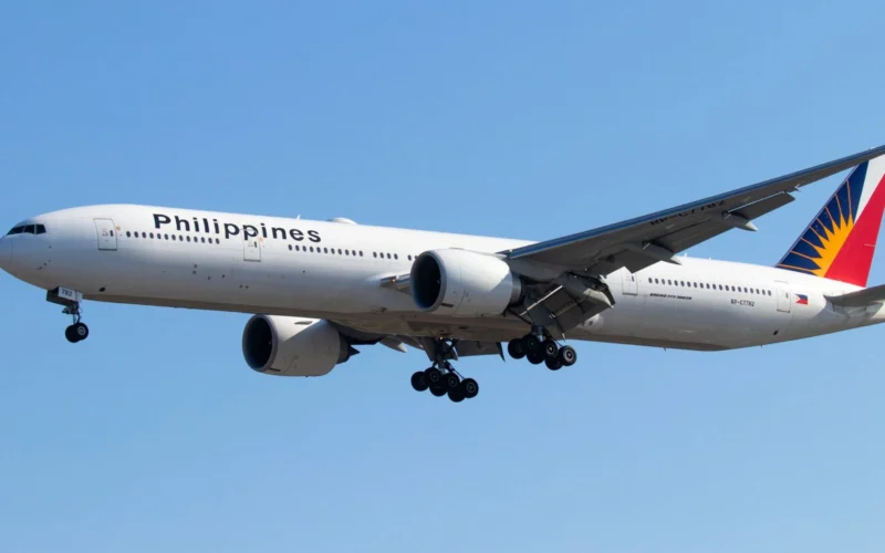 Wide view of a Philippines Airlines jet with landing gear extended flying low against a clear blue sky tail featuring a colorful design