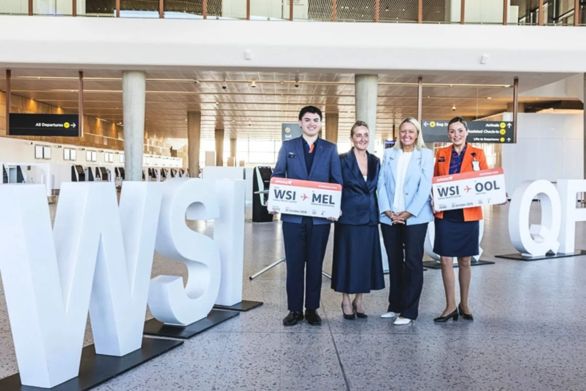 Qantas Jetstar confirm flights from Western Sydney Airport Four airline staff posing with oversized boarding pass signs in a modern airport terminal beside large white letters visible in the foreground