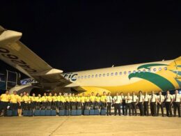 Night time group photo of airline staff in yellow shirts standing in front of a colorful commercial airplane on the tarmac