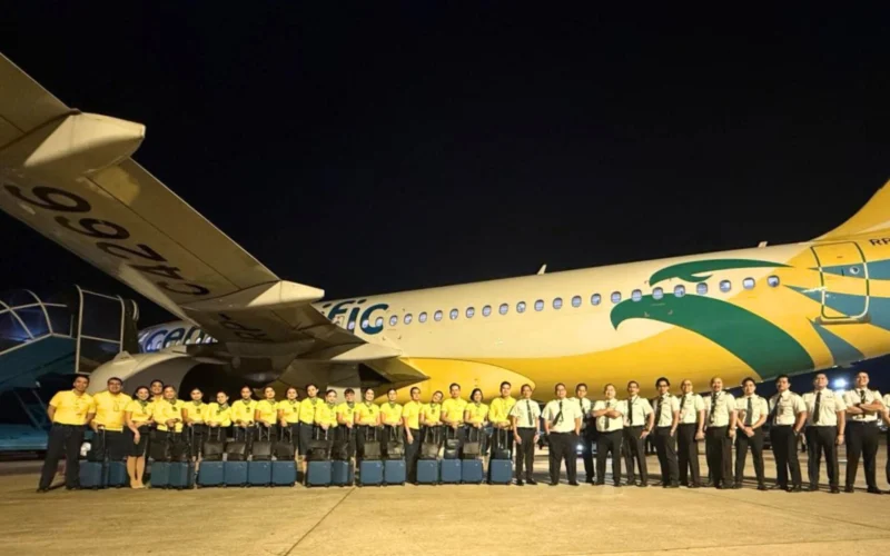 Night time group photo of airline staff in yellow shirts standing in front of a colorful commercial airplane on the tarmac