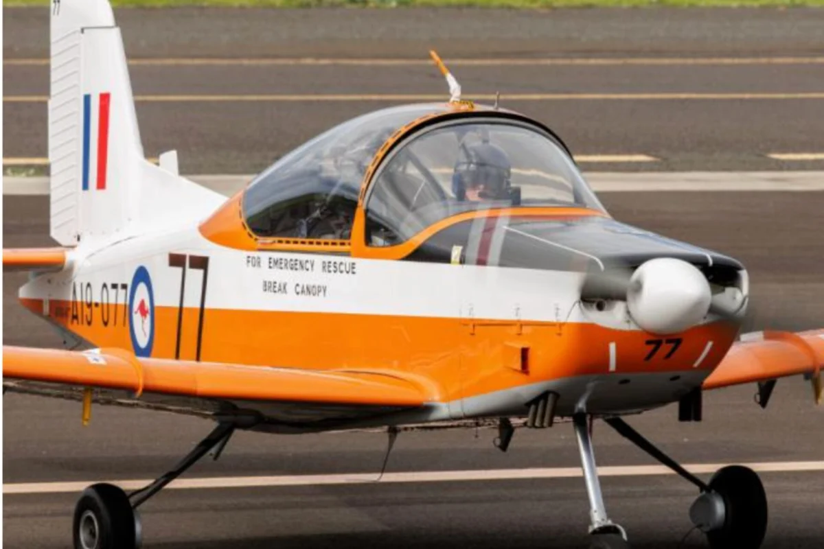 Orange and white rescue aircraft on tarmac with canopy closed text on fuselage reads FOR EMERGENCY RESCUE BREAK CANOPY and tail number 77